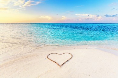 heart drawn on sand of a tropical beach at sunset. clear turquoise ocean. maldives islands.