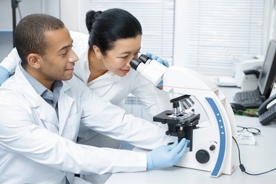 advice from a colleague. professional chemist senior woman looking through the microscope helping her younger male colleague with his research professionalism assistance experience study research 
