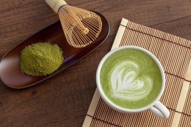 matcha latte art heart shape on top on wooden table with some green tea powder beside and tools for tea making, japanese style