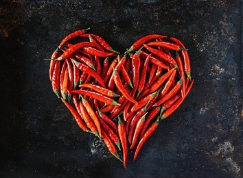 red chili peppers in heart shape, for valentine's day on old black metal background.