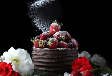 chocolate cake with strawberry and raspberry decorating with flowers on black background