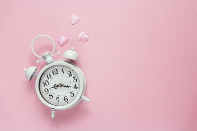 background with white alarm clock and hearts on pink. place for text. top view. time for love and greetings.