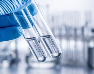 laboratory beakers in analyst's hand in plastic glove.