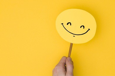 smiling emoji. male hand holding a yellow emotion face with a hand drawn expression