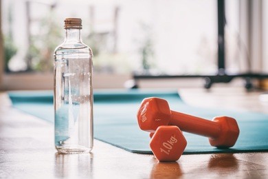 healthy lifestyle and fitness concept. green exercise yoga mat, orange dumbbells and a bottle of water on a wooden floor. 