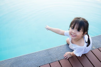 little asian girl looking up and smile sitting near swimming pool alone.