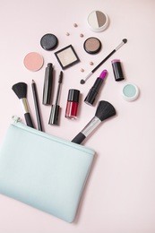 a blue cosmetics bag with makeup products spilling out on to a light pink background