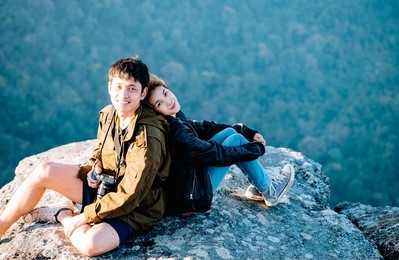 young adult asian couple sitting together enjoys rise to the top of the mountain with light of evening