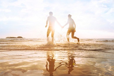 happy young couple having fun on the beach at sunset, water splash, enjoying life