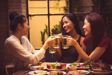 women are drinking beer and the clink glasses in a restaurant.