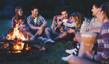happy friends playing music and enjoying bonfire in nature