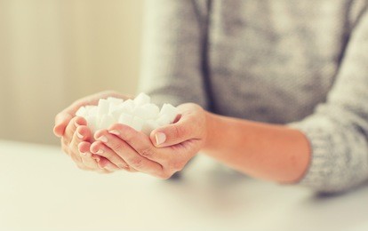 food, junk-food, diabetes and unhealthy eating concept - close up of white lump sugar in woman hands
