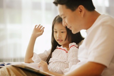 father and daughter, sitting side by side, looking at book
