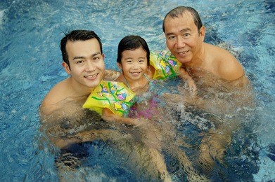 father, grandfather and young girl in a swimming pool, looking at camera
