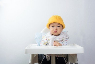 asian baby sitting in high chair white background,baby angry