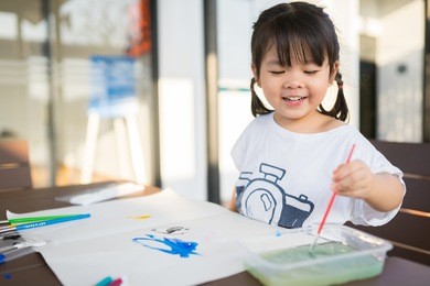 little asian girl painting with paintbrush and colorful paints