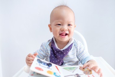 cute little asian toddler baby boy holding and reading book, kid sitting on high chair, happy kid concept