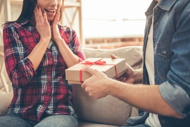 handsome young man is giving a present to his lovely girlfriend while they are sitting on couch at home