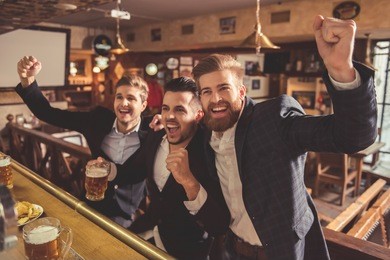handsome businessmen are drinking beer, cheering and smiling while resting at the pub