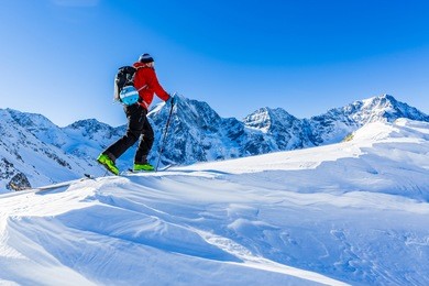 mountaineer backcountry ski walking up along a snowy ridge with skis in the backpack. in background blue sky and shiny sun and zebru, ortler in south tirol, italy.  adventure winter extreme sport. 