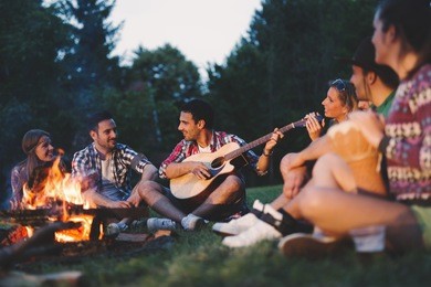 happy friends playing music and enjoying bonfire in nature