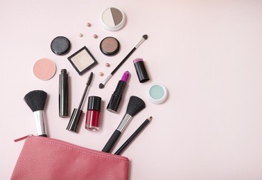 a pink leather make up pouch with cosmetic beauty products spilling out on to a pastel background, with blank space at side