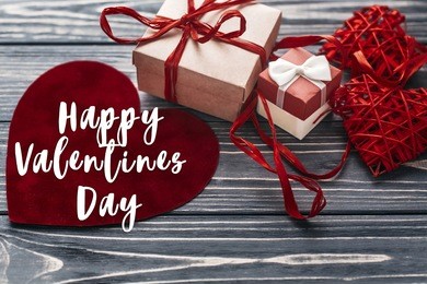 happy valentines day text sign card. stylish hearts and craft present and ribbons on black rustic wooden background. concept. greeting card with space for text. 