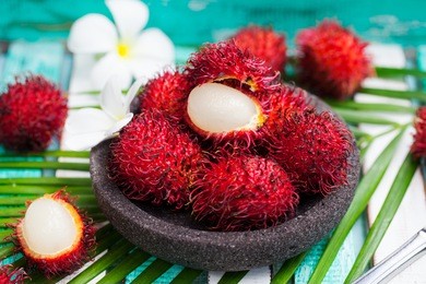 fresh rambutans in a grey stone bowl on wooden colorful background.