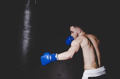 young handsome boxer in blue boxing gloves boxing on black baclground