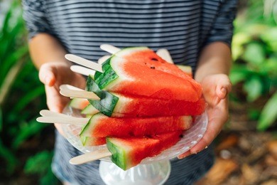 summer vegetables. woman holding slices of watermelon on a stick.