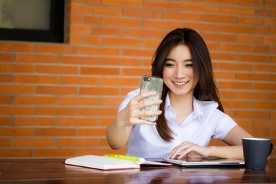 portrait of thai adult student university uniform beautiful girl using her smart phone selfie
