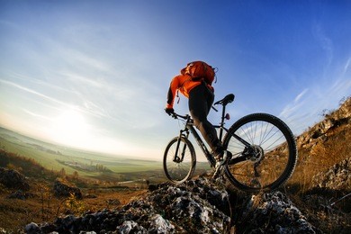 back view of a man with a bicycle and red backpack against the blue sky. cyclist rides a bicycle. rear view people collection. backside view of person. blue sky background and mound.