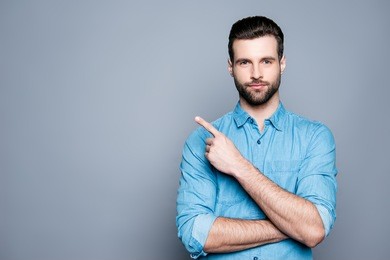 handsome smiling bearded man pointing away on gray background.