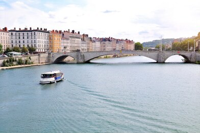 boat sailing on the saone river with the bonaparte bridge and houses in lyon france. horizontal composition