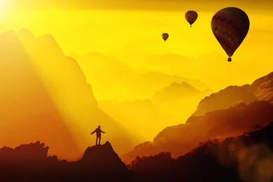 silhouette of young traveler standing on top of mountain with amazing fantasy sunset with hot air balloons.travel lifestyle success concept,adventure active vacation outdoor,happiness freedom emotion.