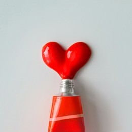 red paint in shape of a heart on white paper background. flat lay. love concept.