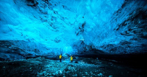 blue crystal ice cave and human figures beneath the glacier in iceland