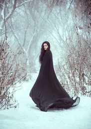 the girl a demon walks alone. she is wearing a long, black traveling cloak.