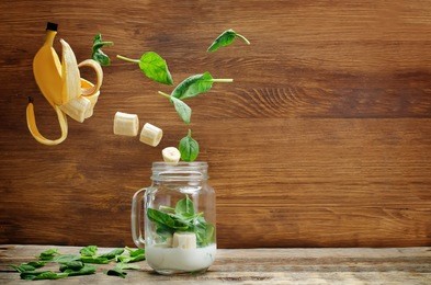 spinach banana smoothie with flying slices on a wood background. toning. selective focus