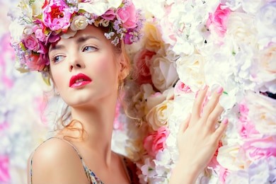 beautiful romantic young woman in a wreath of flowers posing on a background of roses. inspiration of spring and summer. perfume, cosmetics concept.