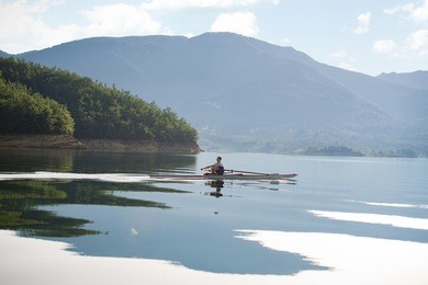 a young single scull rowing competitor paddles on the tranquil lake