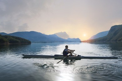 a young single scull rowing competitor paddles on the tranquil lake