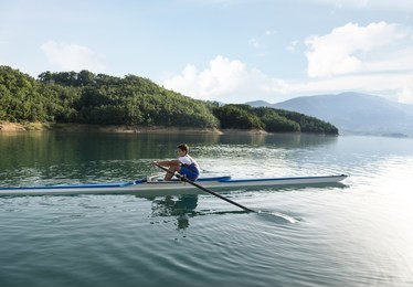 a young single scull rowing competitor paddles on the tranquil lake