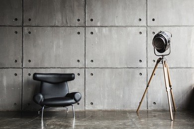 loft interior mock up photo. grey block wall with leather black chair and vintage light source lamp. background photo with copy space for text. 