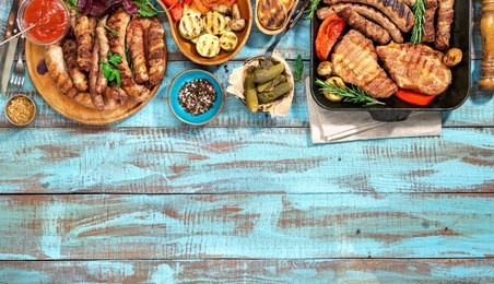 variety of grilled food on the blue wooden table on a sunny day, grilled steak, grilled sausage and grilled vegetables. top view. outdoors food concept