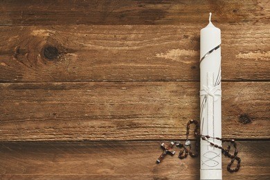 white eucharist candle decorated with a silver cross and rosary on a rustic wood background with copy space, conceptual of communion and easter