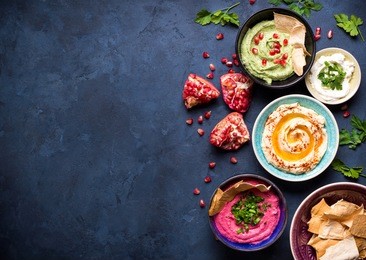 colorful hummus bowls background. different kinds of dips. traditional hummus, herbs hummus, beetroot hummus, spread. assorted meze and dips with crispy pita. space for text. meze and snacks concept