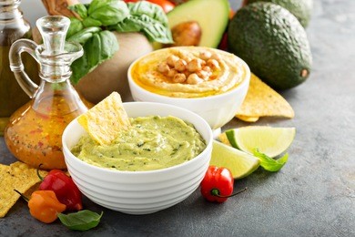 guacamole and hummus in white bowls with vegetables and corn chips