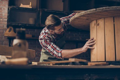 handsome joiner check wood.  stylish young entrepreneur with beautyful hairstyle and saved glasses work at his workstation. he love his job and workplace.