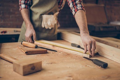closeup photo of  cabinetmaker's tabletop.  craftsman holding ruler  on wooden planknear other tools.